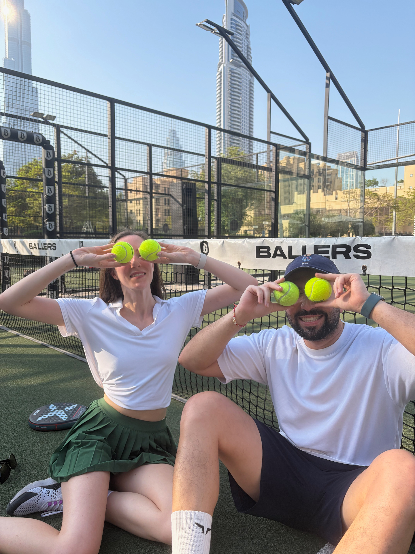 Two players playfully holding padel balls over their eyes